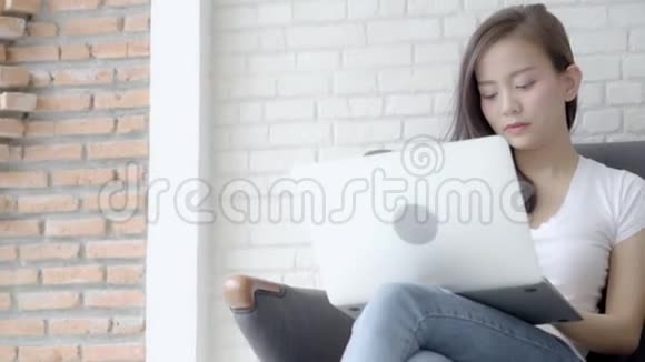 美丽的肖像亚洲年轻女子带着微笑在客厅的沙发上工作视频的预览图