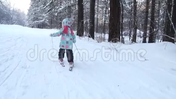 女孩正在学习滑雪她在松软的雪地里慢慢地滑上滑雪板冬天森林里美丽的一天走进去视频的预览图