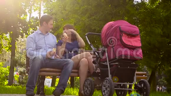 爸爸和妈妈吃冰淇淋和婴儿车一起在公园散步暑假全家放假视频的预览图