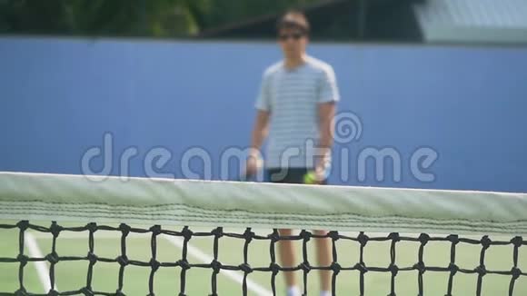 阳光明媚的一天年轻人戴着太阳镜玩网球拍网格前景模糊的慢运动视频的预览图