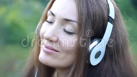 女人用耳机听音乐眼睛紧闭在户外视频的预览图