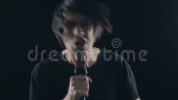 摇滚歌手对着麦克风唱歌然后在黑色背景上摇头摇滚音乐会的概念视频的预览图