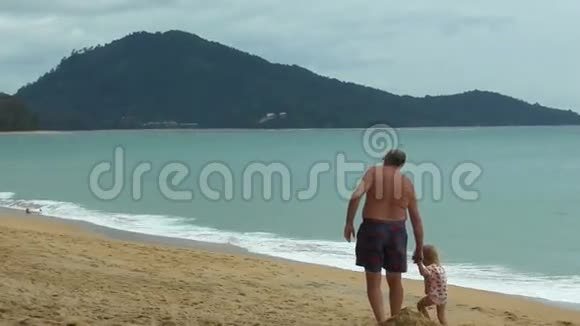 爷爷牵着小女孩的手在海滩上散步视频的预览图