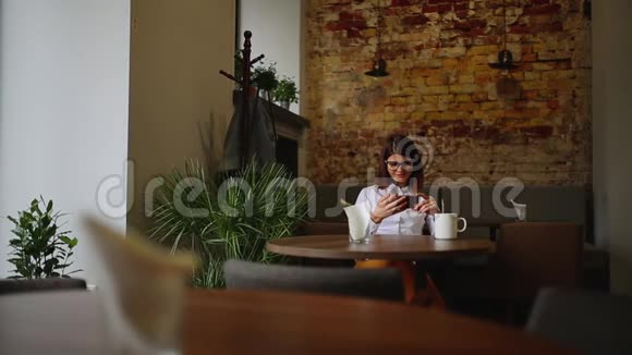快乐的年轻女子坐在咖啡店里用智能手机发短信视频的预览图