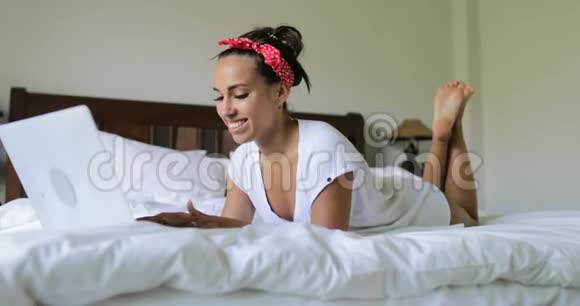 年轻女性用笔记本电脑打字美丽的女孩躺在卧室的床上视频的预览图