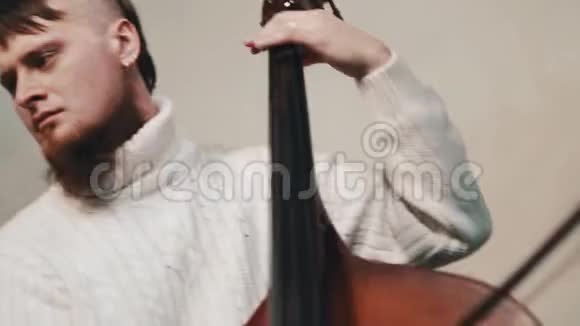 穿着针织高领毛衣的留胡子的年轻音乐家用手提杆玩长角球视频的预览图