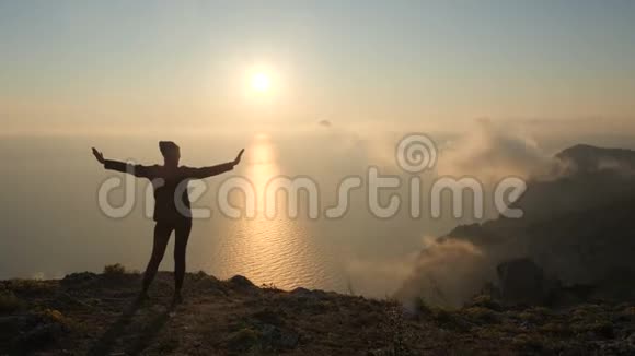 在克里米亚的一座高山上年轻女子伸出双臂在海面上观看一场美丽的戏剧性日落视频的预览图