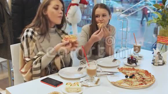 两个年轻的女学生朋友在咖啡馆里吃披萨和聊天在城市街道的背景视图中秋天视频的预览图