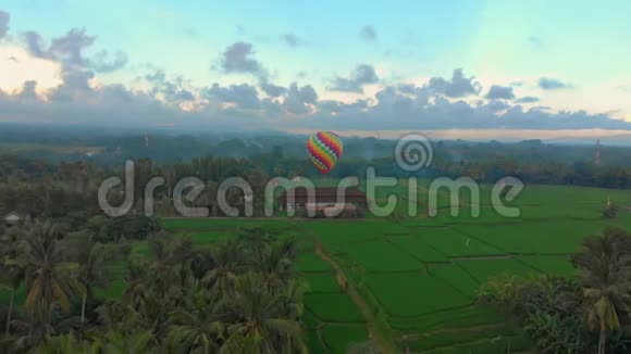 空中拍摄的一个热气球正飞过绿色的大稻田旅行到巴厘岛的概念视频的预览图