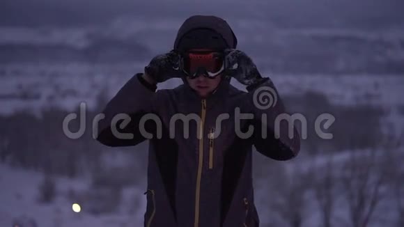 这个年轻人调整他的护目镜以便晚上在斜坡上滑雪视频的预览图