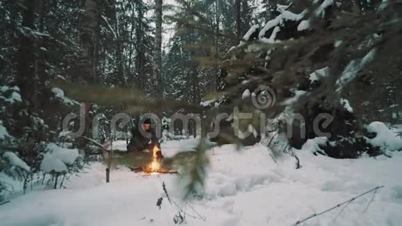坐在森林里篝火前的年轻人试图取暖视频的预览图