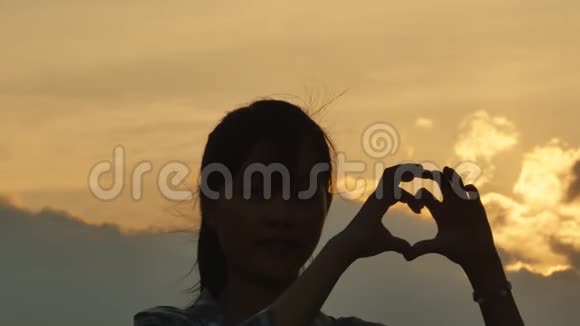 日落时年轻姑娘亲手制作的心轴浪漫的主题视频的预览图