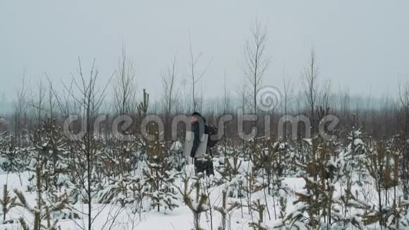 冬天的一天在白雪覆盖的草原灌木丛上散步的年轻人视频的预览图