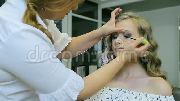 专业化妆师将睫毛膏涂在金发模特的睫毛上视频的预览图
