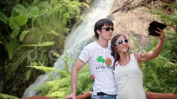 幸福夫妇戴着太阳镜在美丽的瀑布背景下自拍翡翠池和外来植物视频的预览图