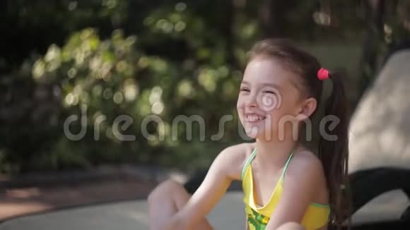 一个穿着泳衣的小女孩正坐在游泳池旁的休息室里笑着视频的预览图