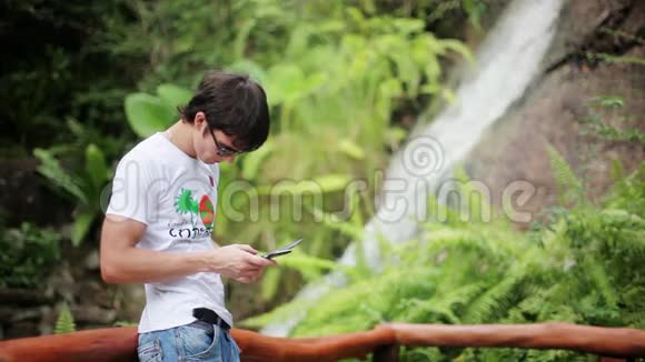 在森林瀑布附近戴着手机太阳镜的人使用智能手机1920x1080视频的预览图