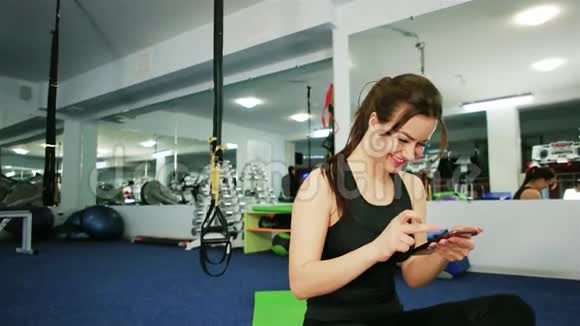 年轻女子在一个现代化的健身房里做健身运动时正在自拍视频的预览图