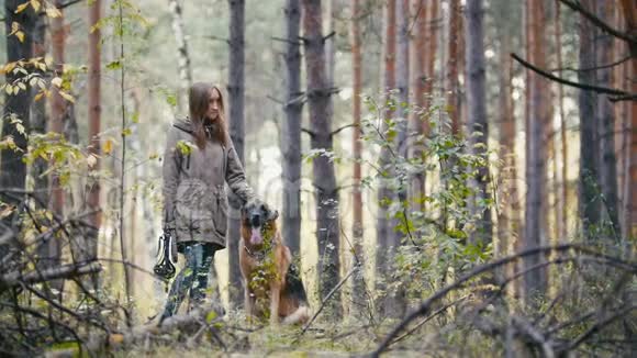 一个年轻漂亮可爱的女人在秋林里散步她的宠物德国牧羊犬站在空地上女孩视频的预览图