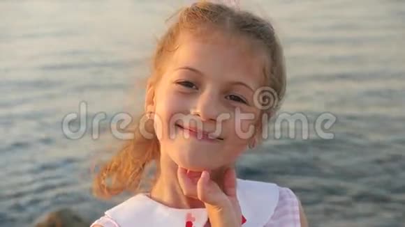 美丽的小女孩在大海的背景下夕阳的微笑露出牙齿视频的预览图