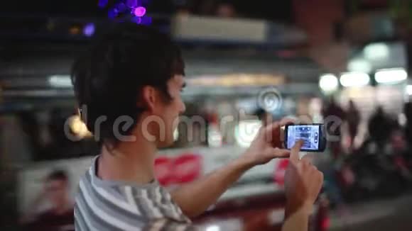 在苏梅岛度假期间带着手机的游客在夜间街上用bokeh灯拍照视频的预览图