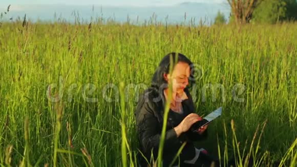 一位年轻的女士正在公园里的一块平板电脑上工作她正坐在计划中的绿草上视频的预览图