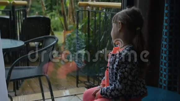 小女孩坐着从里面看后院想玩但外面下着大雨视频的预览图
