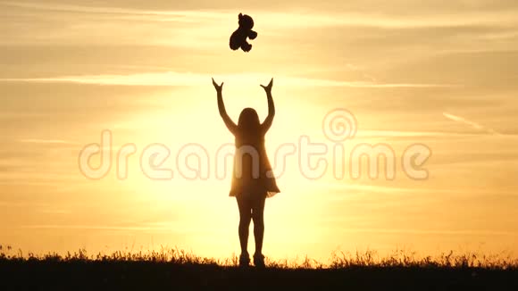 日落时分带着泰迪熊的小女孩抱着熊娃娃熊看日落的女孩剪影概念大梦想视频的预览图