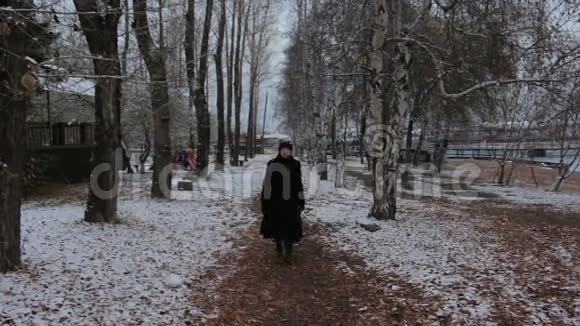 穿着黑色衣服的女孩在寒冷的阴天在冬天的公园里散步视频的预览图