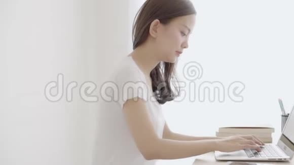 美丽的年轻自由职业亚裔女性微笑着在笔记本电脑上工作在办公桌前讲手机视频的预览图