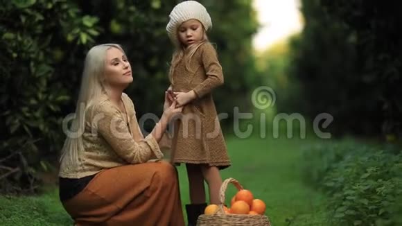 在绿色的阳光果园里带着一篮子水果的绿色草地上带着小女孩的慈爱的母亲的侧面景色全高清视频的预览图