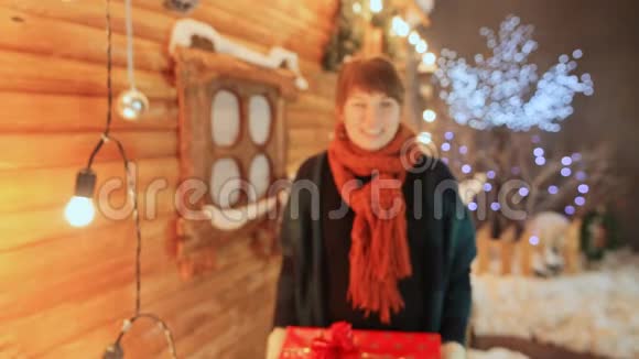 这个女孩在木制童话屋的背景下滑稽和开玩笑地给观众一份礼物圣诞节和新视频的预览图