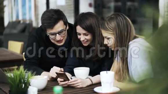 三个朋友正在外面的咖啡馆里看智能手机上的视频视频的预览图