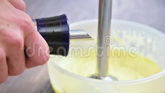 在塑料碗里用搅拌器将自制蛋黄酱的混合物搅拌橄榄油视频的预览图