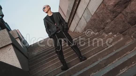 穿着摇滚服装的雌雄同体秃头女孩踩在楼梯外面视频的预览图
