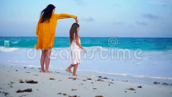 温暖的夜晚可爱的小女孩和年轻的母亲在热带海滩日落时在海滨跳舞的小女孩视频的预览图