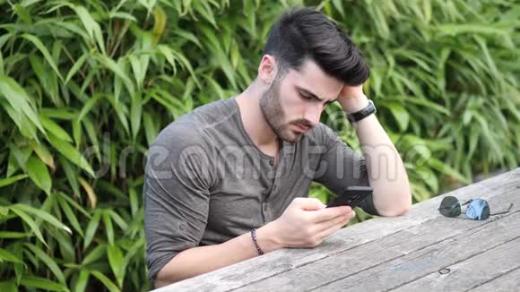 坐在长凳上用手机的年轻人视频的预览图