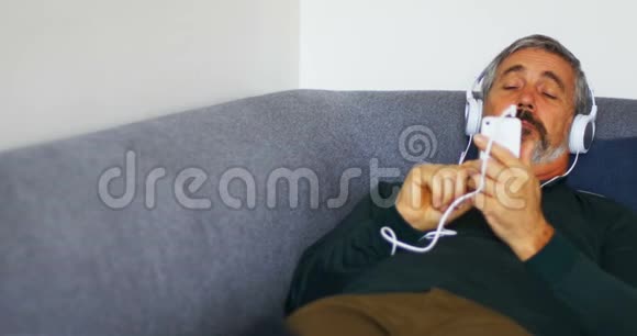 男人躺在沙发上用手机听音乐视频的预览图