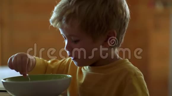 厨房里的孩子在桌子旁吃饭快乐的孩子快乐的婴儿用勺子吃食物视频的预览图