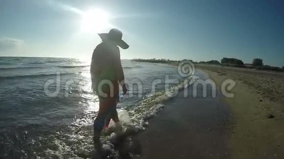 戴帽子的女人在日落时沿着海浪散步视频的预览图