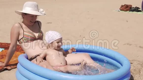 在阳光明媚的日子里妈妈和女儿坐在游泳池里一起在海滩上玩视频的预览图