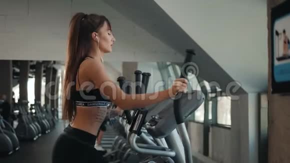 漂亮的深色头发的运动健身女性在有氧运动机上锻炼运动女性锻炼双手腿走路视频的预览图