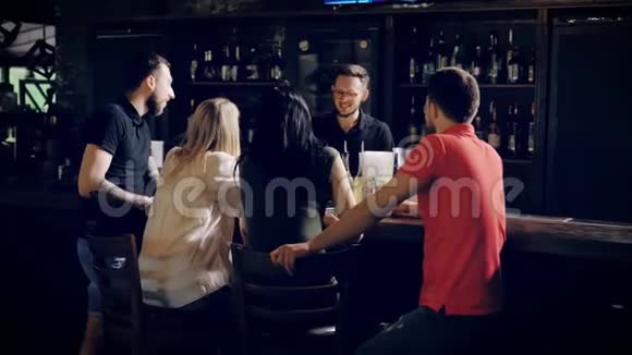 四个年轻的朋友在酒吧柜台放松在木桌的另一边与酒吧老板交谈公司视频的预览图