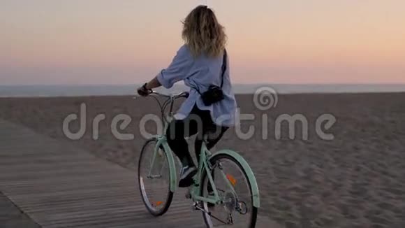年轻的金发摄影师女性在海滩上骑自行车视频的预览图
