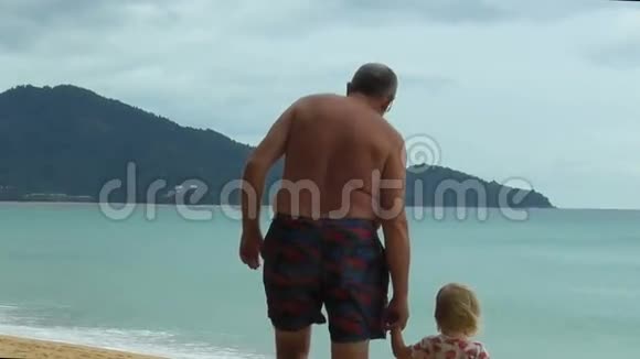 爷爷牵着小女孩的手在海滩上散步视频的预览图