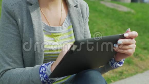年轻女子在公园里休息享受数码平板电脑视频的预览图