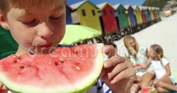 男孩一边吃西瓜一边家人坐在沙滩上视频的预览图