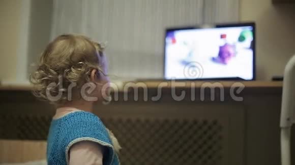一个卷发的金发小女孩在看手提电脑上的卡通视频的预览图