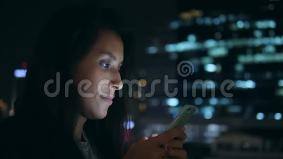 年轻的微笑女人在城市的夜晚在手机上发短信4K使用智能手机的混血女孩视频的预览图