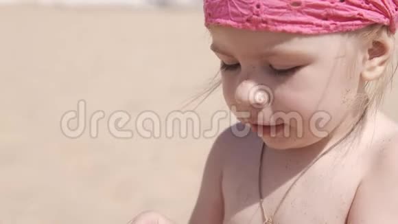 小可爱的女孩在海滩上玩沙子和贝壳在UHD关闭视频的预览图
